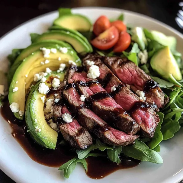 Plate piled with steak, avocado chunks, tomatoes, and greens.