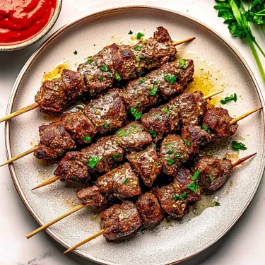 A plate of meat skewers with a bowl of sauce.