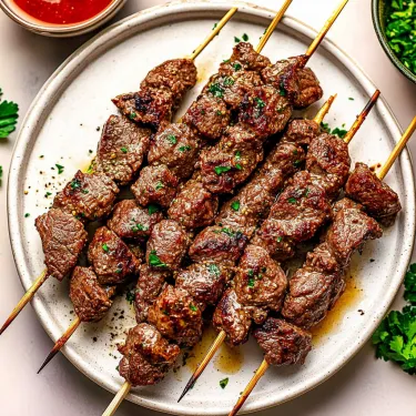 A plate of meat skewers with a bowl of sauce.