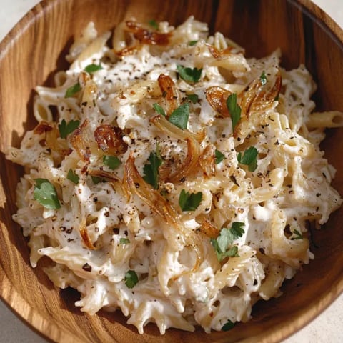 A bowl piled high with pasta, onions, and cheesy bits.